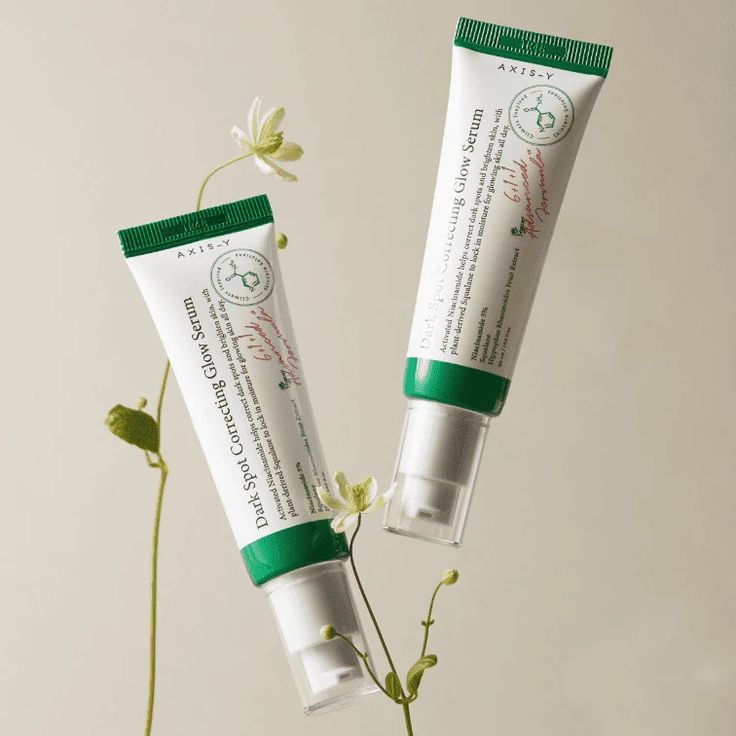 Axis-Y Dark Spot Correcting Glow Serum tubes surrounded by delicate greenery, showcasing the skincare product.