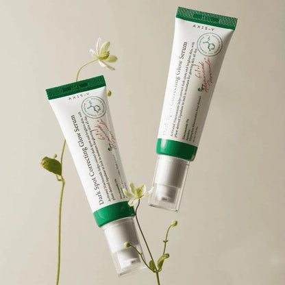 Axis-Y Dark Spot Correcting Glow Serum tubes surrounded by delicate greenery, showcasing the skincare product.
